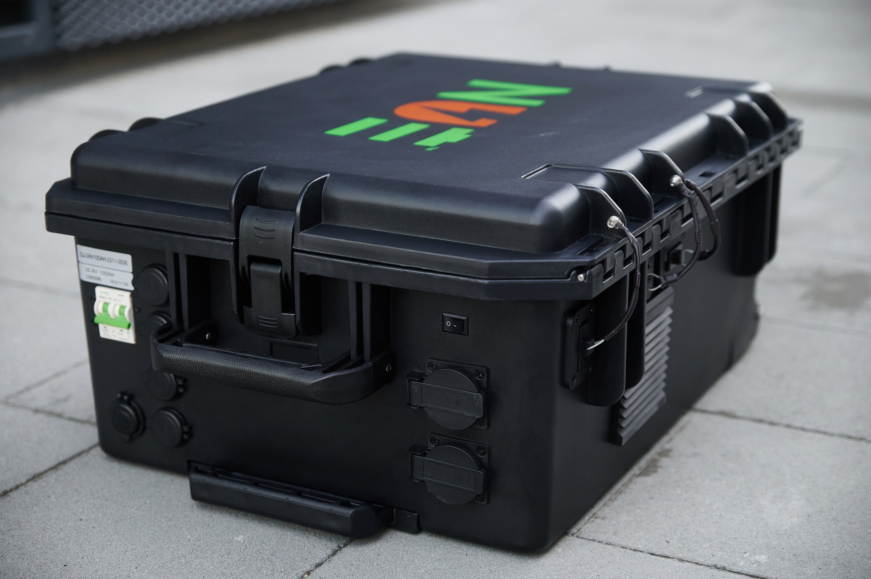 Black NUE portable power case with multiple outlets, a sturdy handle, and ventilation, placed on a concrete surface.