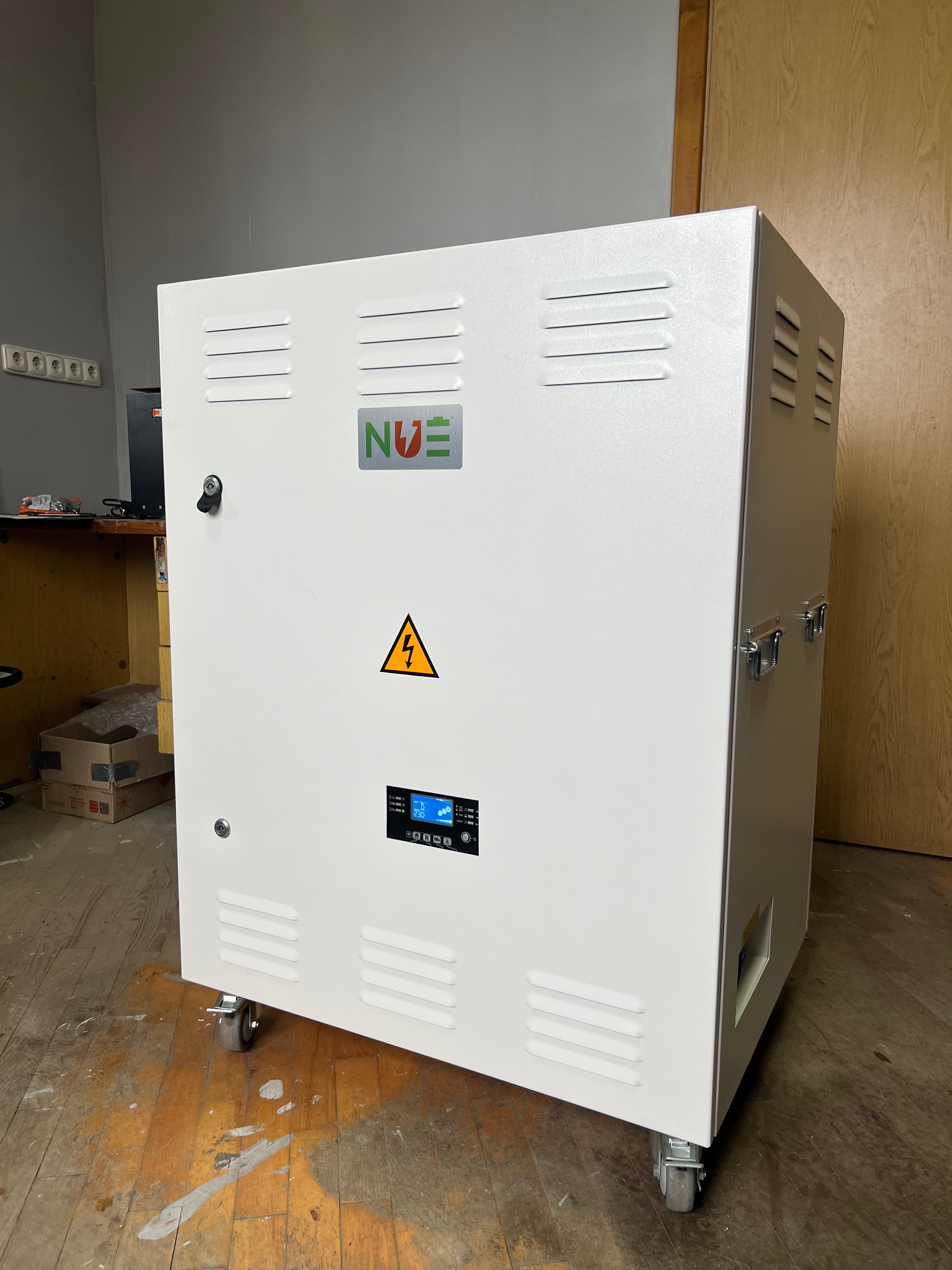 White NUE energy storage unit on wheels, featuring a control panel, ventilation grilles, and a high-voltage warning symbol.
