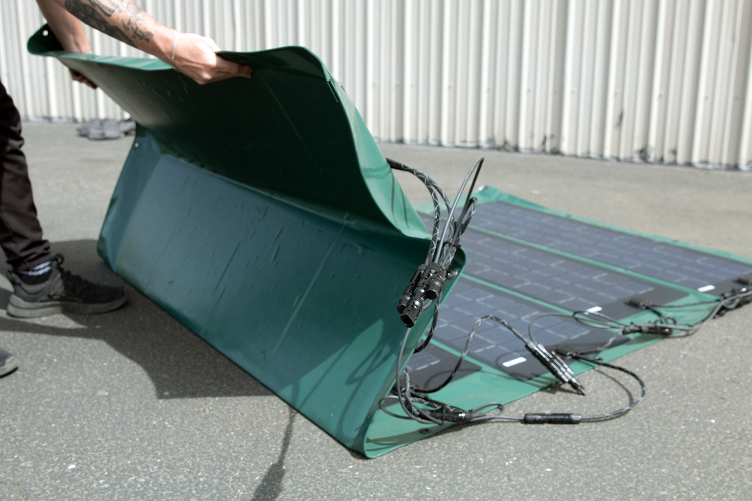 A person lifting a green solar panel with attached cables.