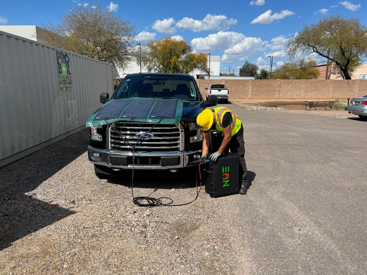 A worker in safety gear is setting up a solar panel on the hood of a truck